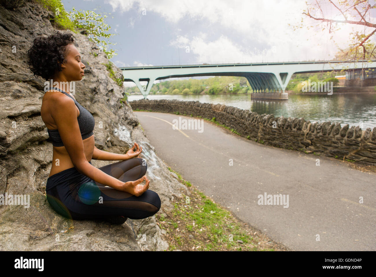 Donna seduta zampe trasversale su roccia meditando Foto Stock