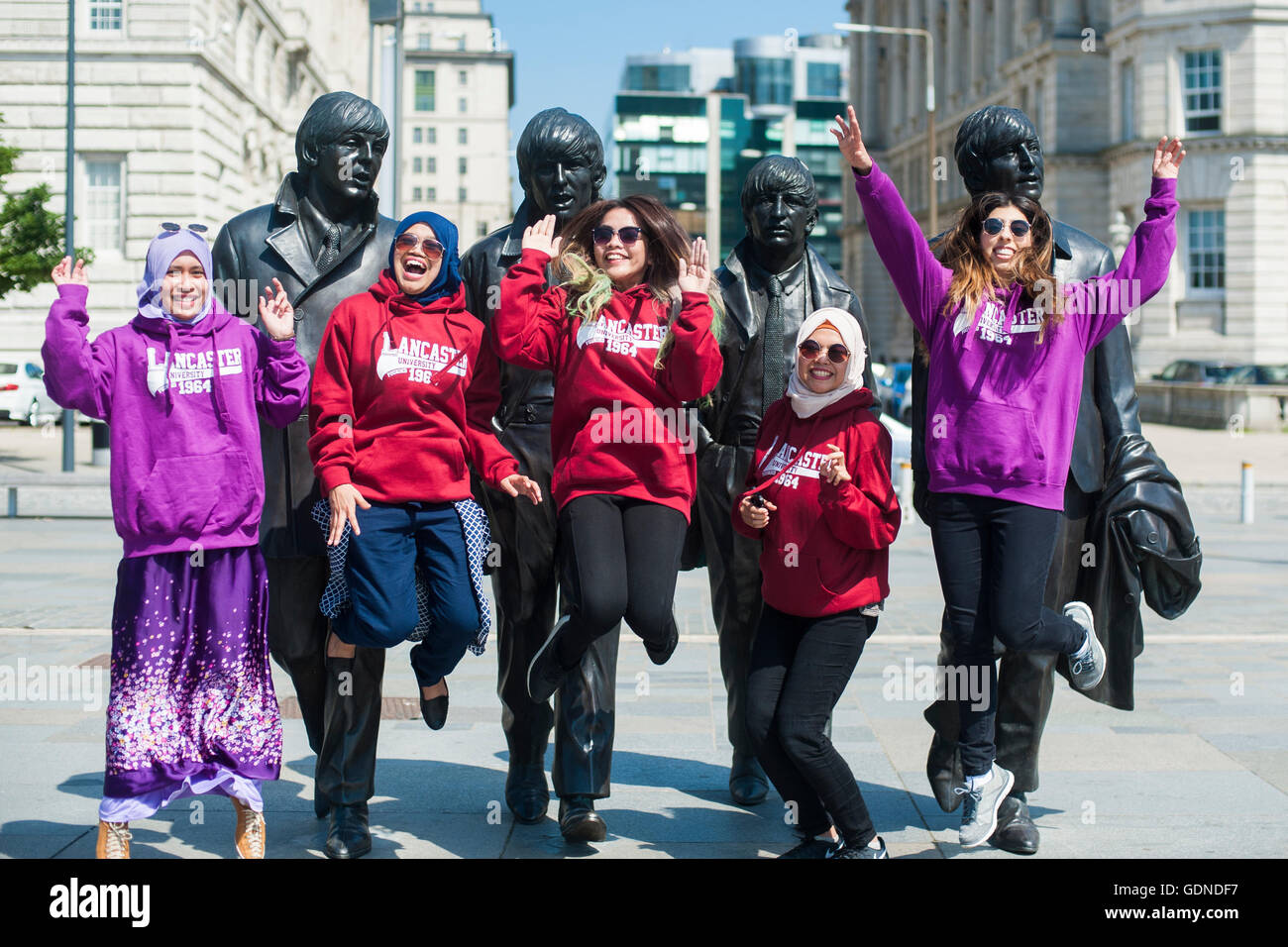 Un gruppo di giovani felici gli studenti di diverse minoranze etniche salta in alto nella parte anteriore del Beatles statue in Liverpool Regno Unito Foto Stock