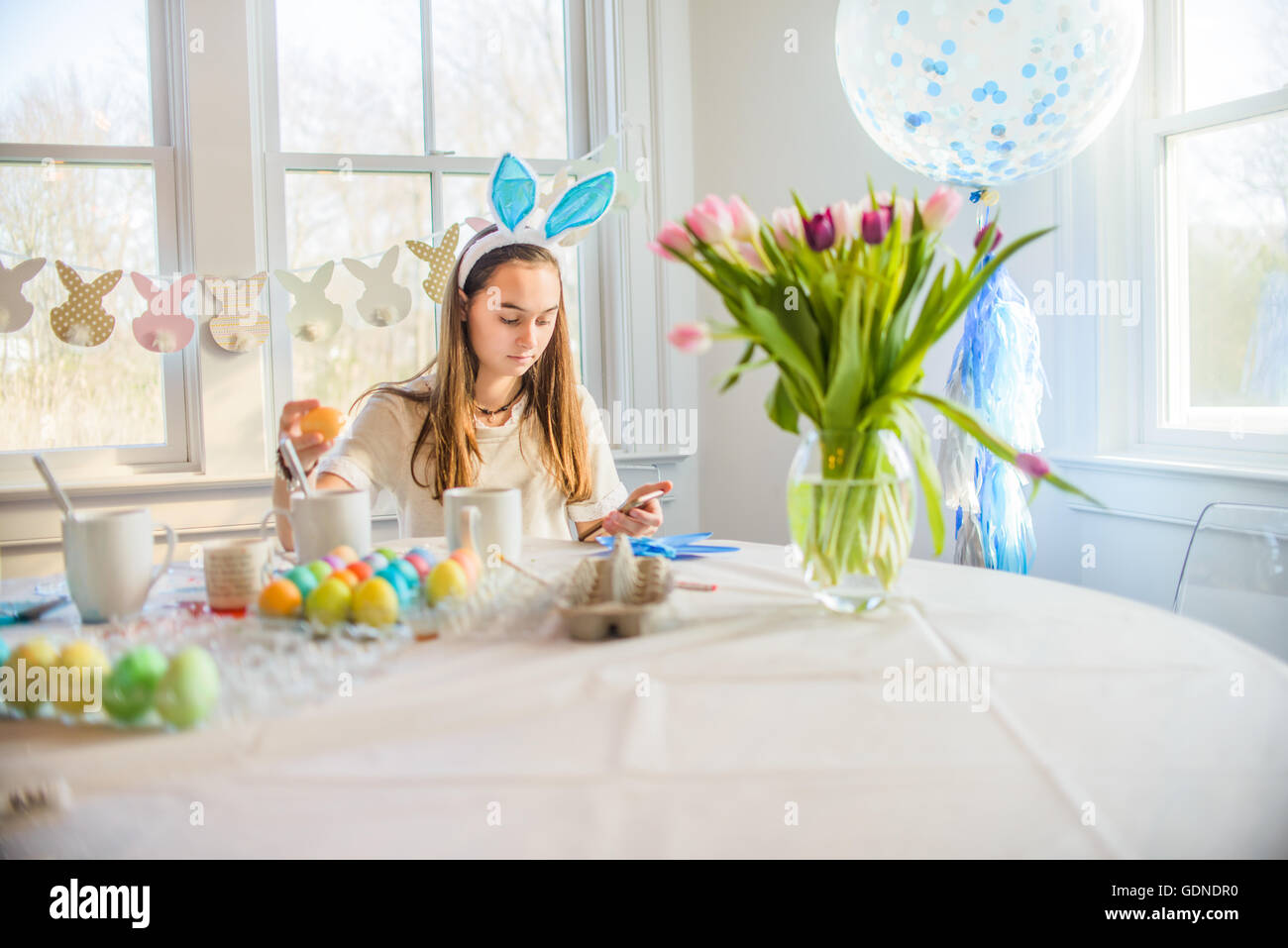 Ragazza adolescente la lettura di testi mentre la tintura di uova sode per la Pasqua a tavola Foto Stock