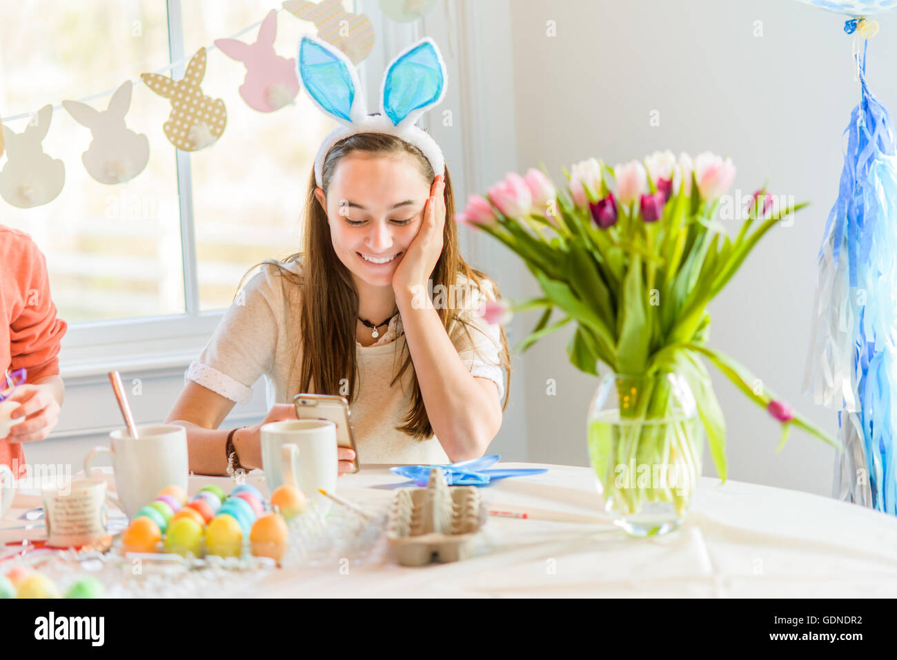 Ragazza adolescente a tavola la lettura di testi sullo smartphone mentre la tintura di uova sode per la Pasqua Foto Stock