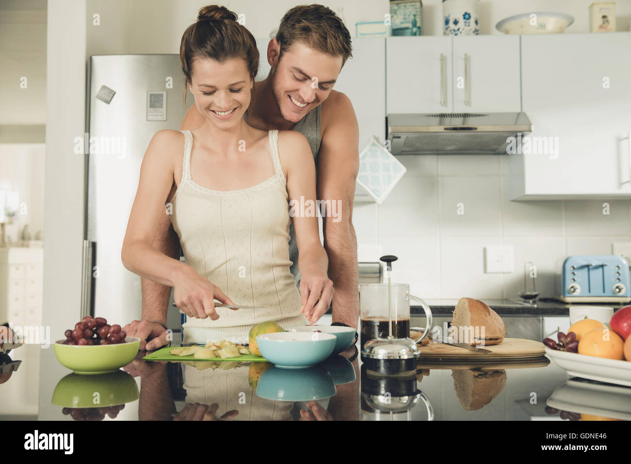 Romantico giovane uomo guarda la ragazza mentre prepara la colazione in cucina Foto Stock