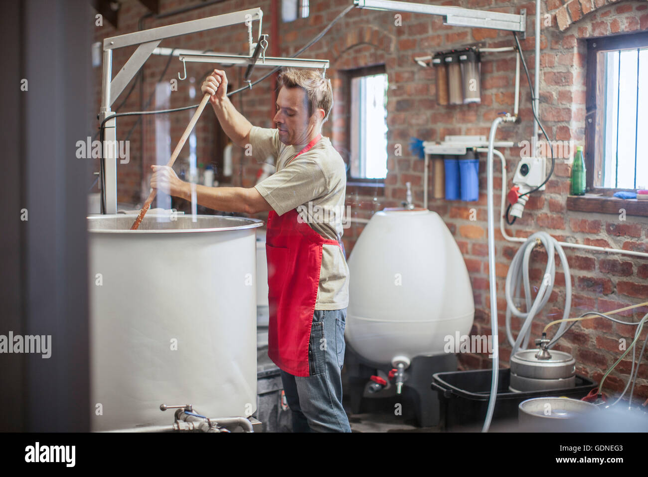 Uomo in microbirreria agitazione del serbatoio di fermentazione Foto Stock