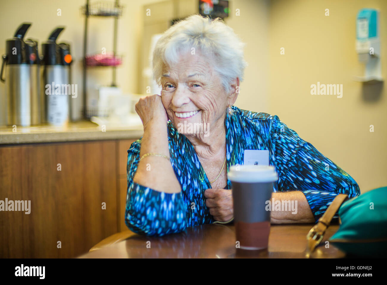 Grigio donna dai capelli al tavolo guardando sorridente della fotocamera Foto Stock