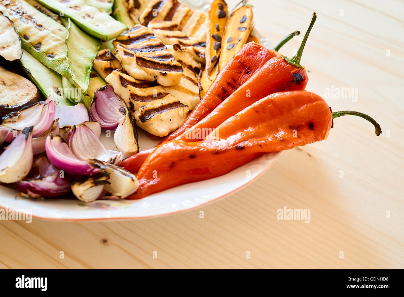 Vista ravvicinata su una piastra con verdure arrosto e il formaggio halloumi, su di un tavolo di legno, Piatto sano Foto Stock