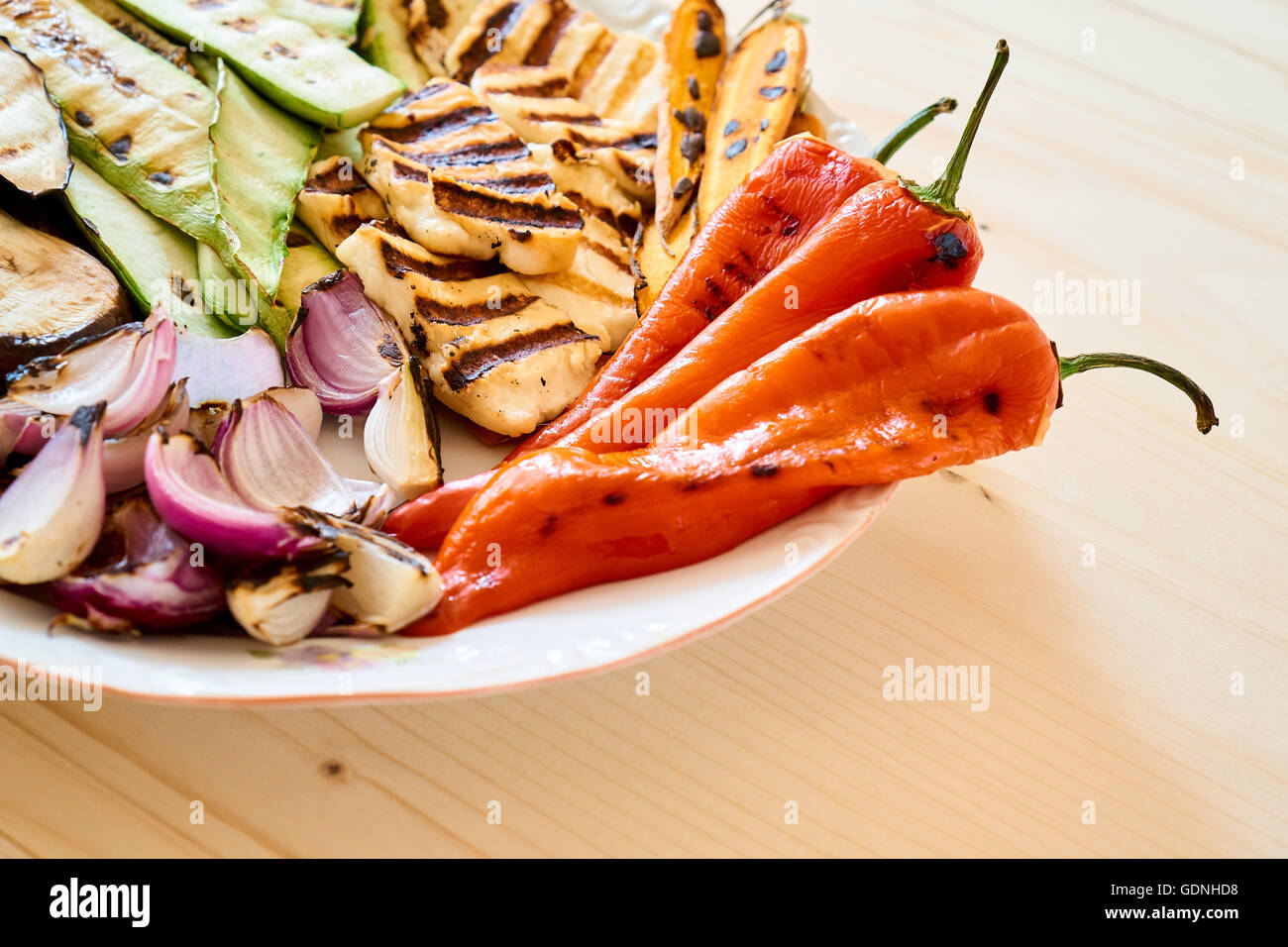Vista ravvicinata su una piastra con verdure arrosto e il formaggio halloumi, su di un tavolo di legno, Piatto sano Foto Stock