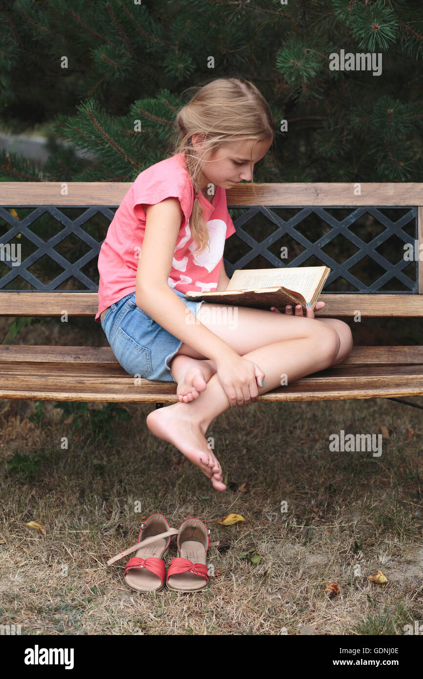 Ragazza la lettura di un libro su una panchina nel parco Foto Stock