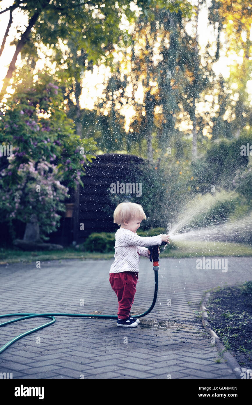 Carino Baby girl irrigare il giardino utilizzando un tubo da giardino. Foto Stock