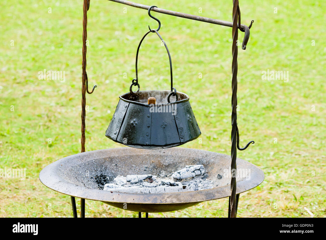 Cucina Outdoor pentola appesa sopra di legno bruciato e cenere. Pentola è fatta a mano in ferro annerito con rivetti. Foto Stock