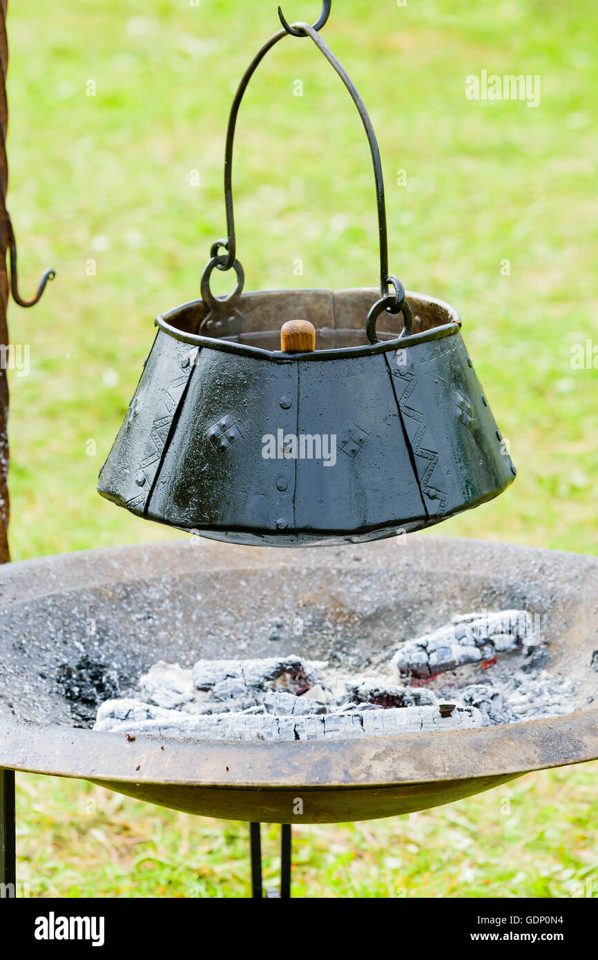 Cucina Outdoor pentola appesa sopra di legno bruciato e cenere. Pentola è fatta a mano in ferro annerito con rivetti. Foto Stock
