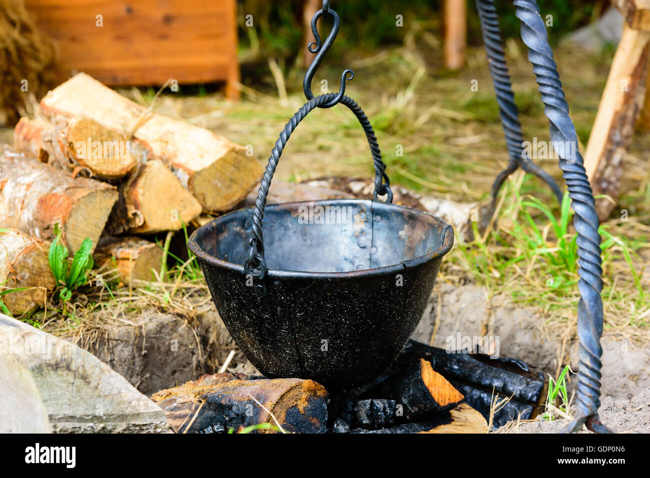 Vuoto cucina outdoor pentola appesa sopra di legno bruciato e cenere. Pentola è fatta a mano in ferro annerito con rivetti. Foto Stock