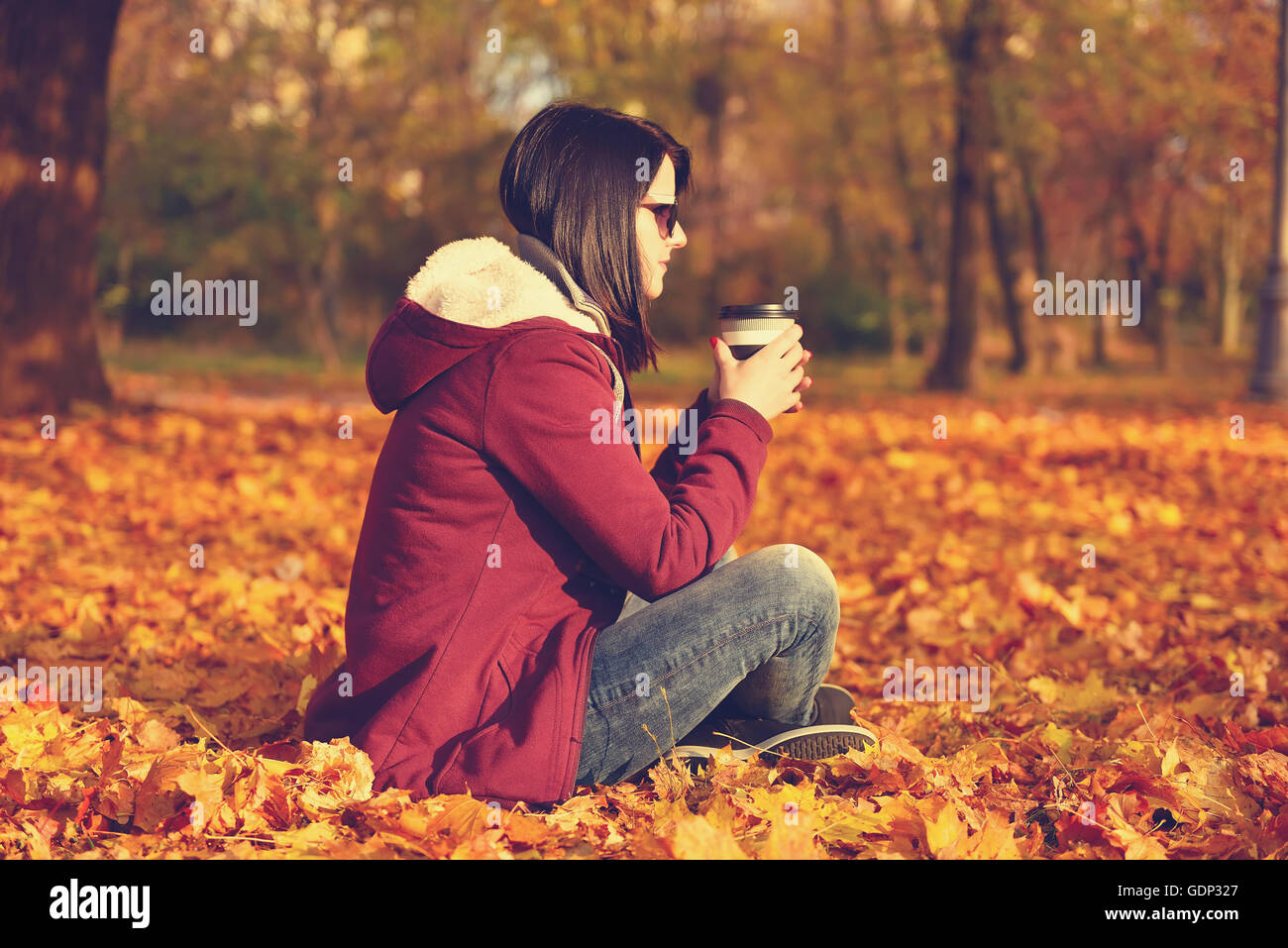 Ragazza con tazza di caffè seduti su foglie di giallo. Foto d'epoca Foto Stock