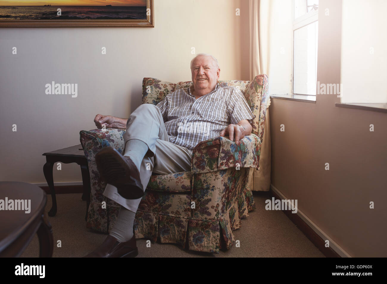 Ritratto di una rilassata anziano uomo seduto su di una poltrona a casa vecchia Foto Stock