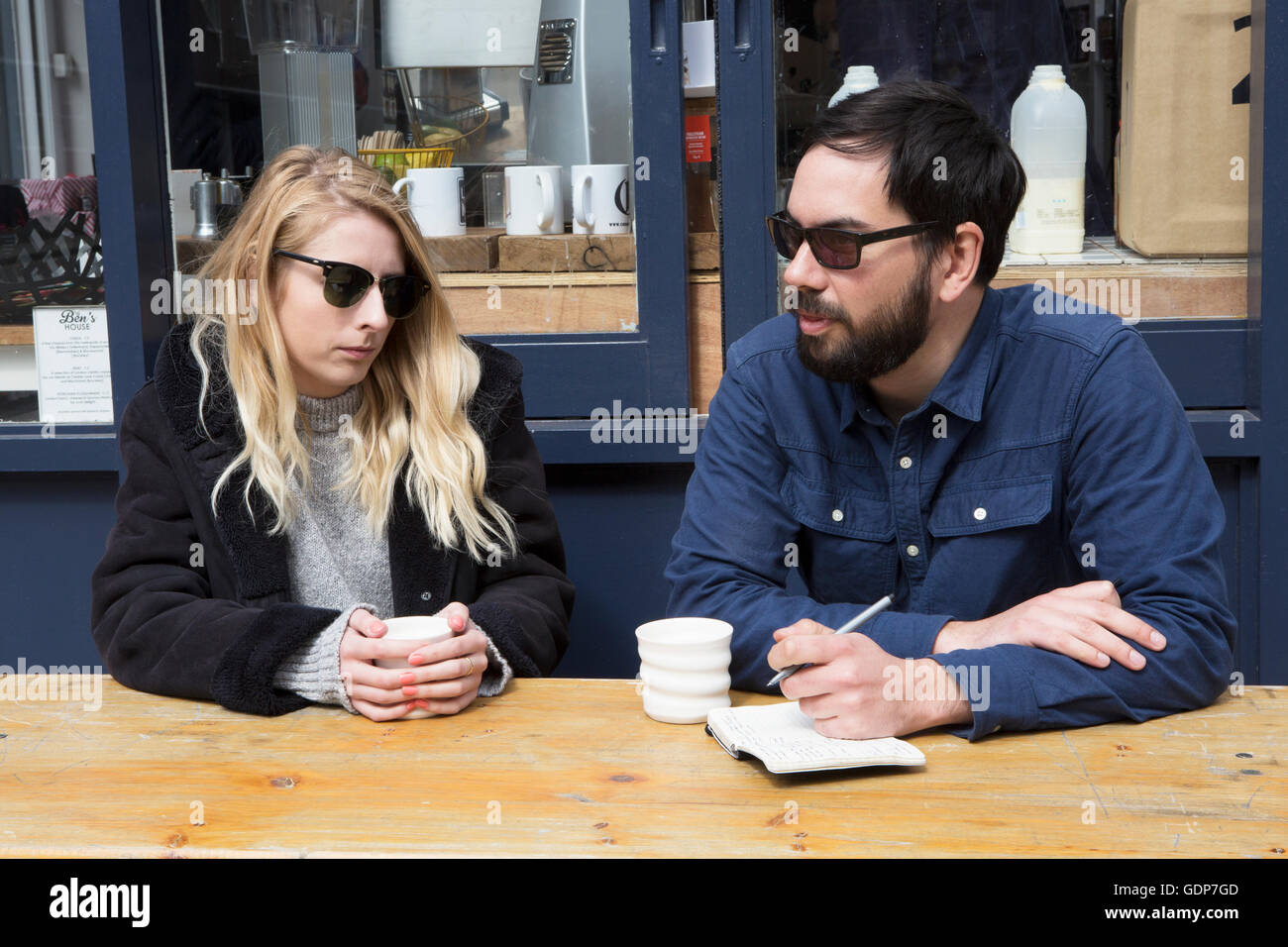 Giovane seduti al cafè sul marciapiede tabella iscritto nella nota prenota Foto Stock