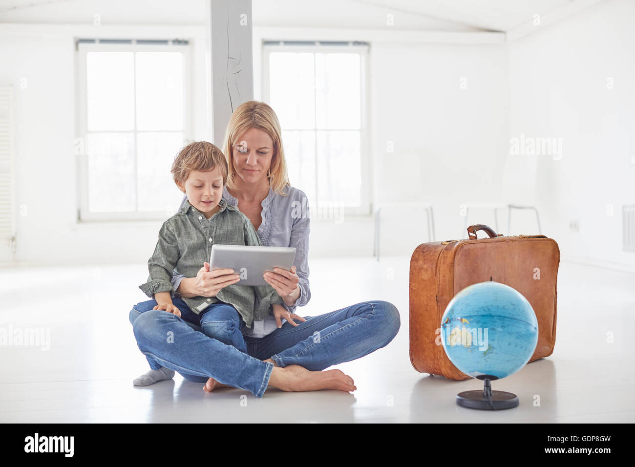 Donna matura e figlio seduti sul pavimento guardando a tavoletta digitale Foto Stock