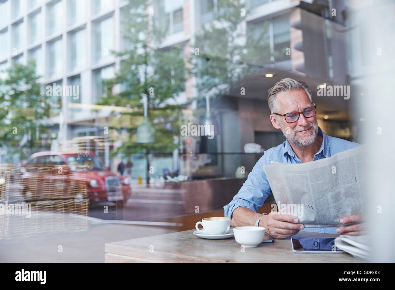 Uomo maturo in seduta cafe, leggendo il giornale, street riflessa nella finestra Foto Stock