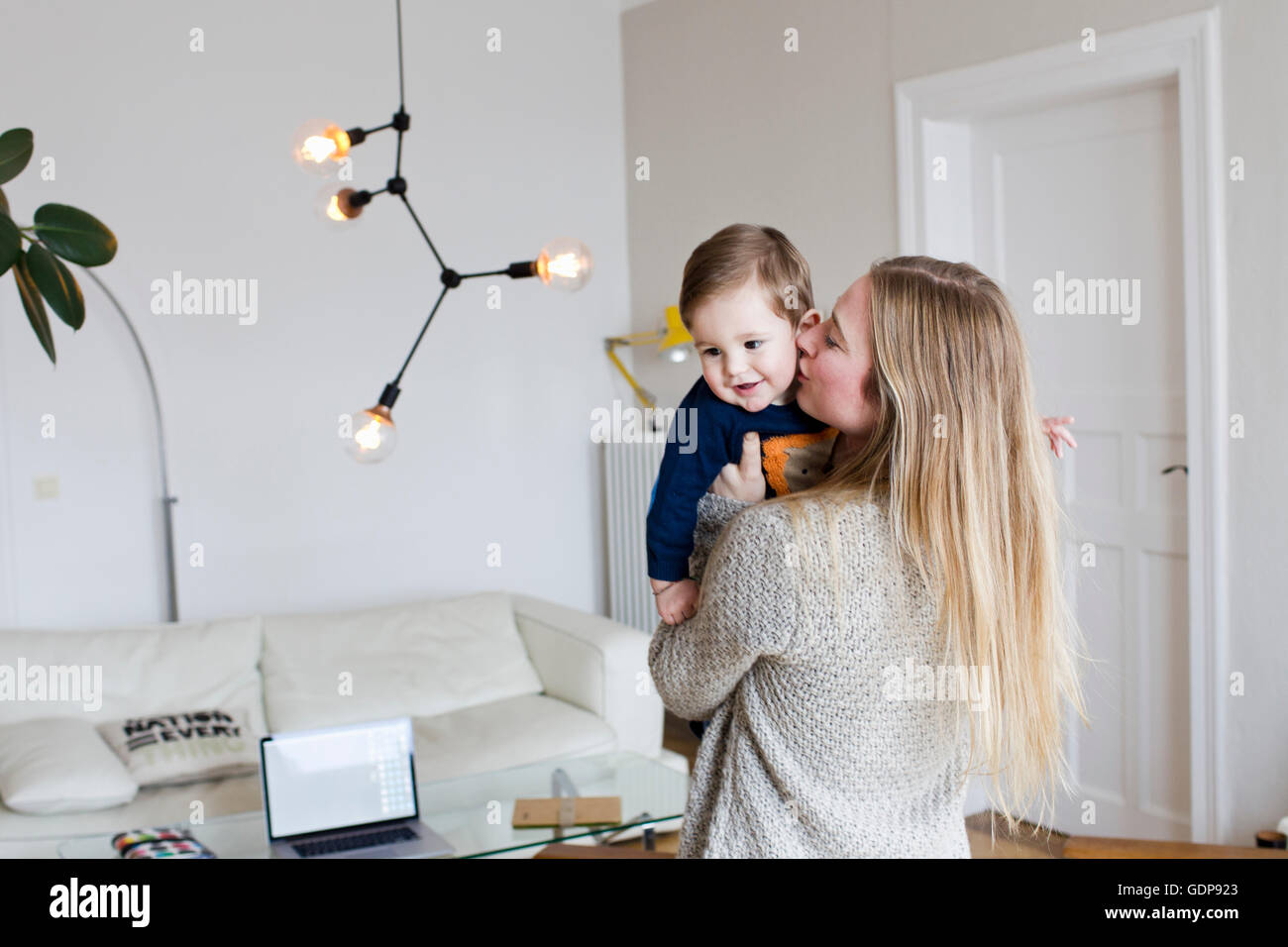 Metà donna adulta kissing baby figlio sulla guancia in salotto Foto Stock