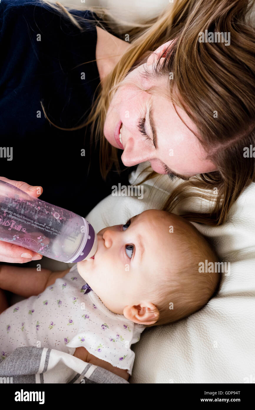 Vista aerea della metà donna adulta biberon per baby figlia sul divano Foto Stock
