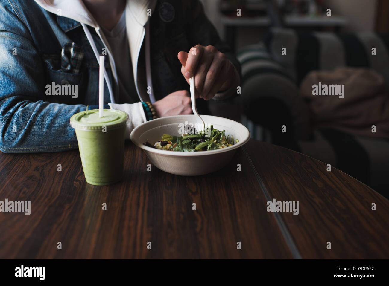 Giovane uomo seduto a tavola, mangiare insalata, metà sezione Foto Stock