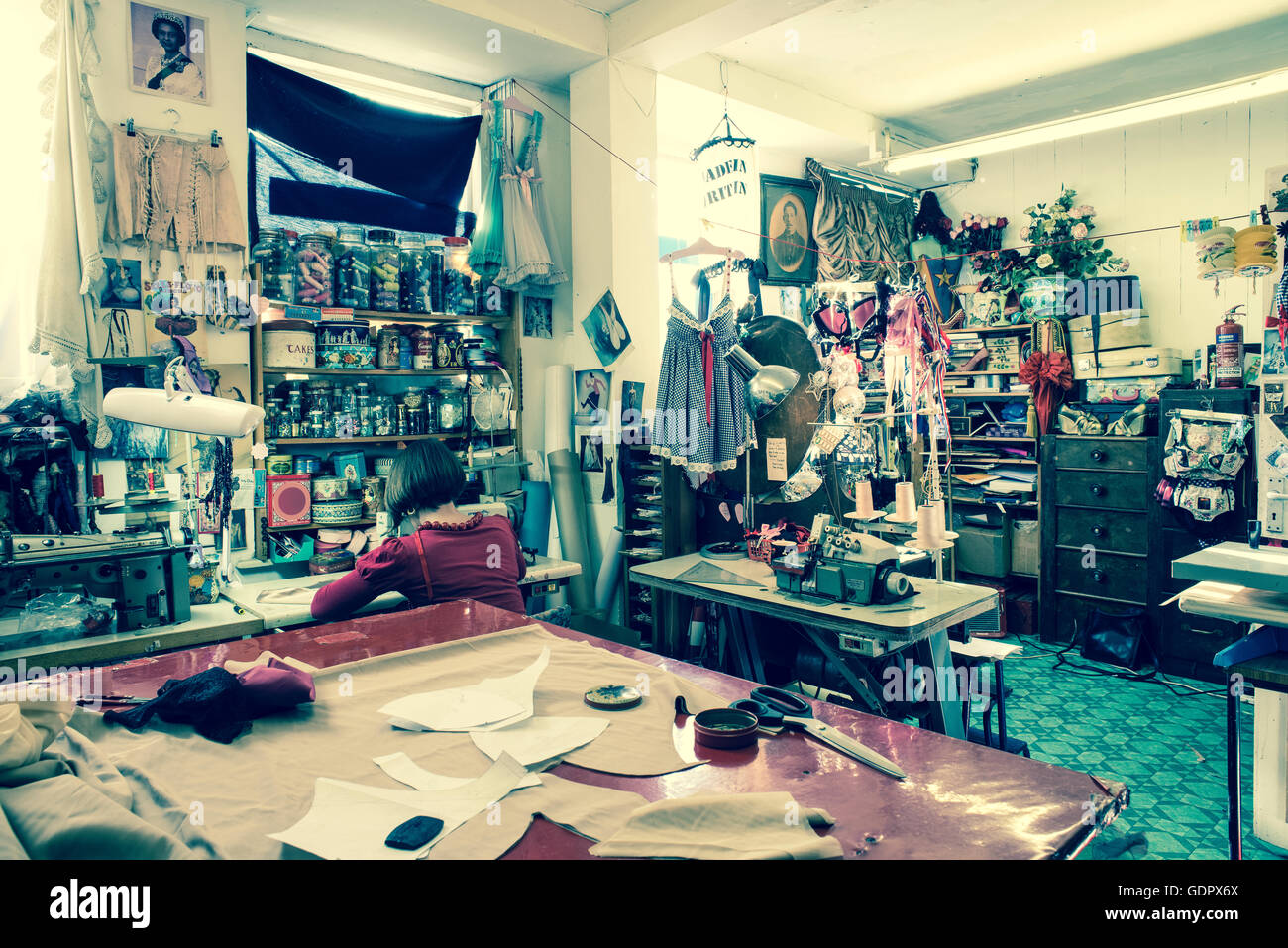 All'interno di un negozio di sartoria con una sarta con la schiena girata lavorando su una macchina da cucire. Foto Stock