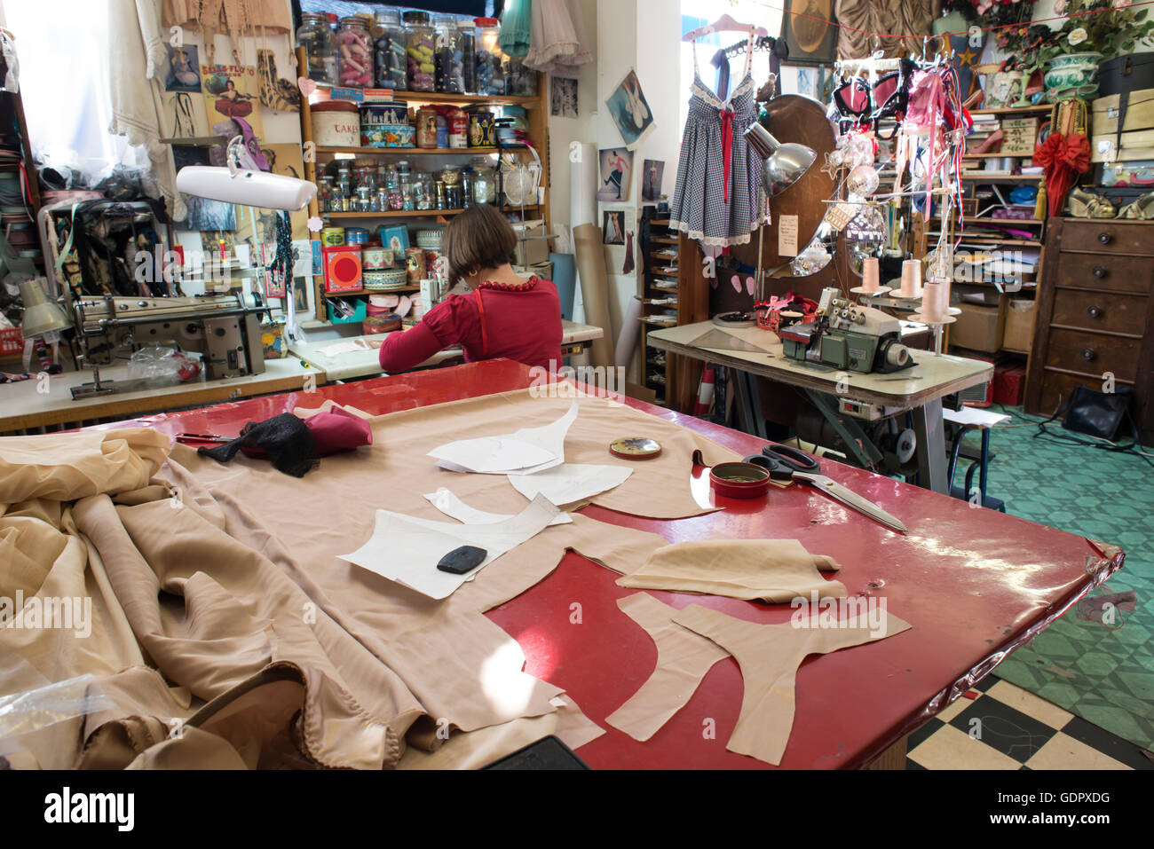 Un grande sarto il tavolo da taglio con sarta lavorando e tutto l'interno del negozio di abbigliamento in background. Foto Stock