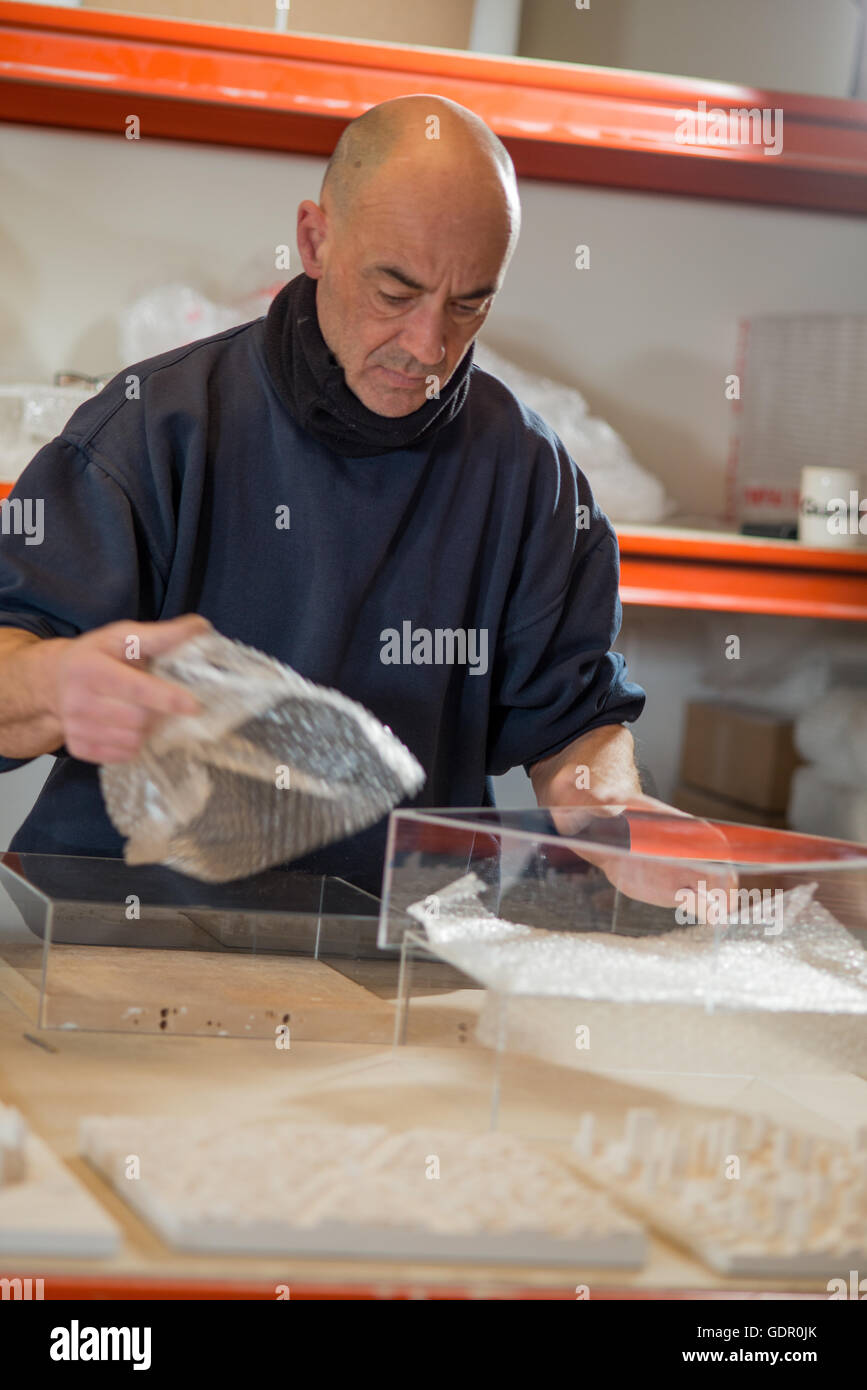 Un uomo in un maglione scuro di prendere un pezzo di Bubble wrap off un trasparente acrilico caso per intonaco la città in miniatura di modelli. Foto Stock