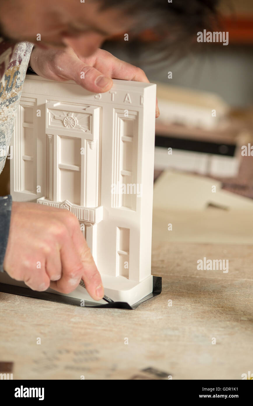 Un uomo nero a fresare carta posizionati al di sotto della base di un modello in gesso edificio utilizzando una lama di precisione Foto Stock