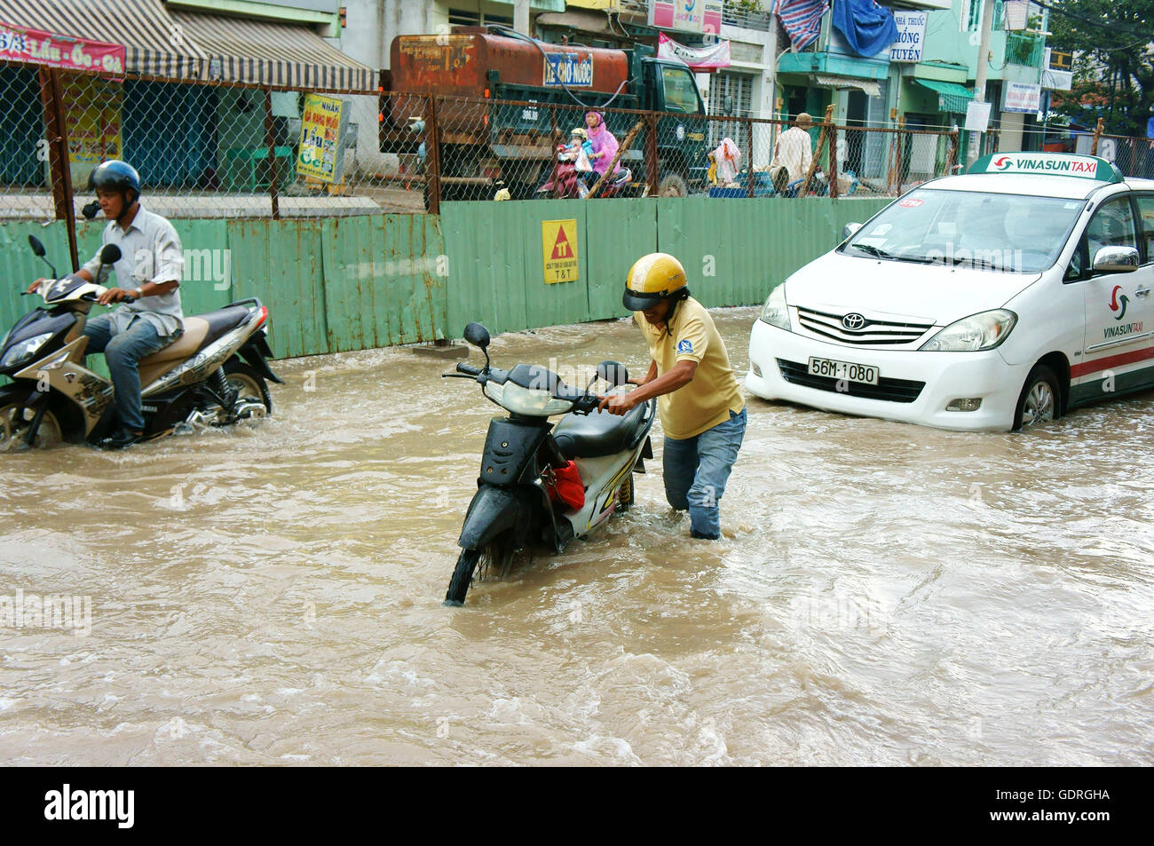 Gruppo del popolo vietnamita ride moto, biciclette in movimento su strada allagata dopo la pioggia Foto Stock