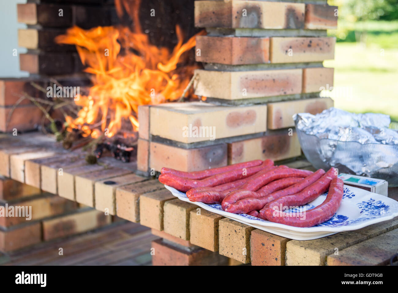Merguez salsicce su una piastra, barbecue in muratura con fuoco e fiamme Foto Stock