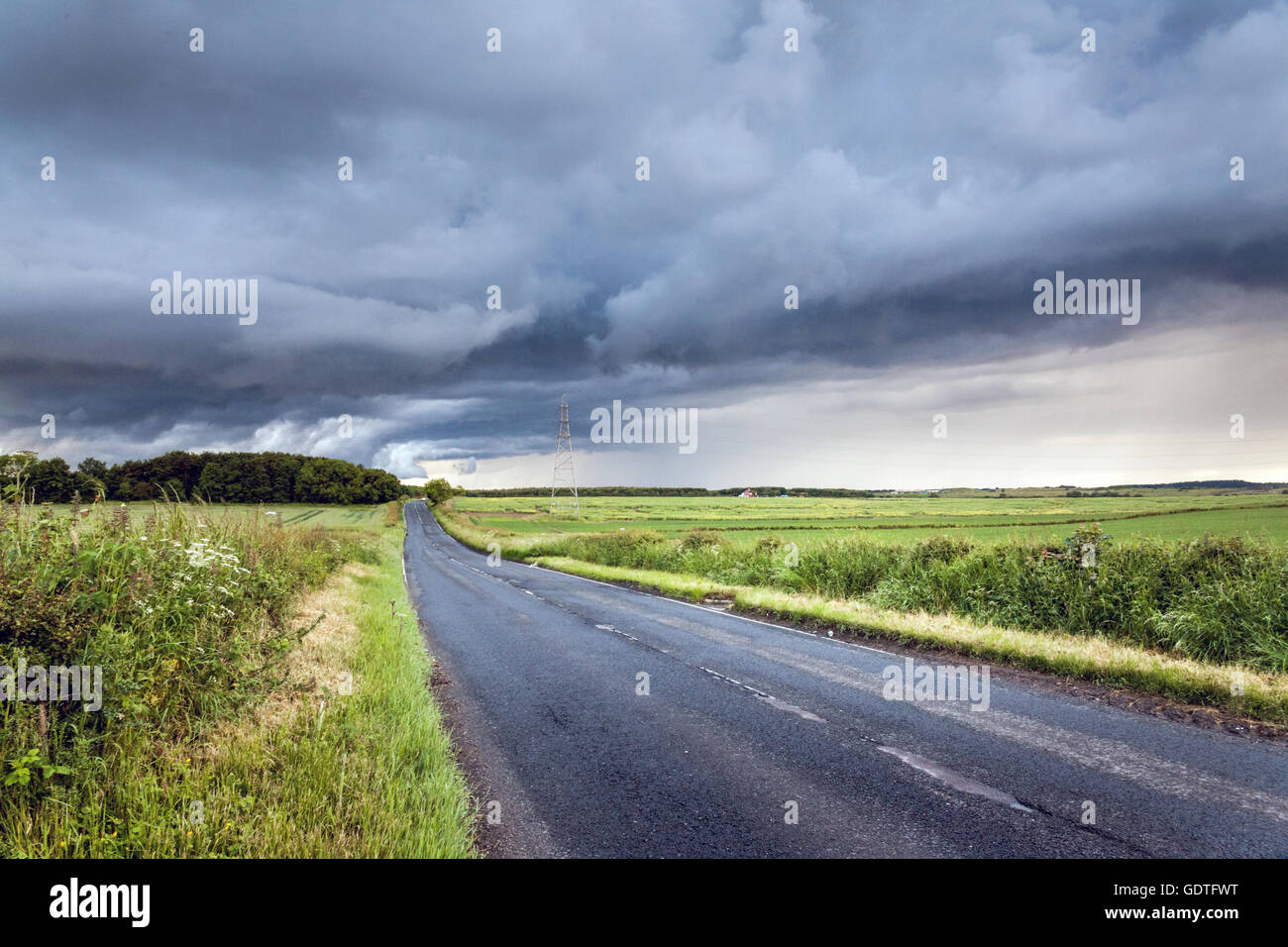 Un paese desolato strada che conduce all'orizzonte e un imminente tempesta davanti in Northumberland, Inghilterra del Nord Est. Foto Stock