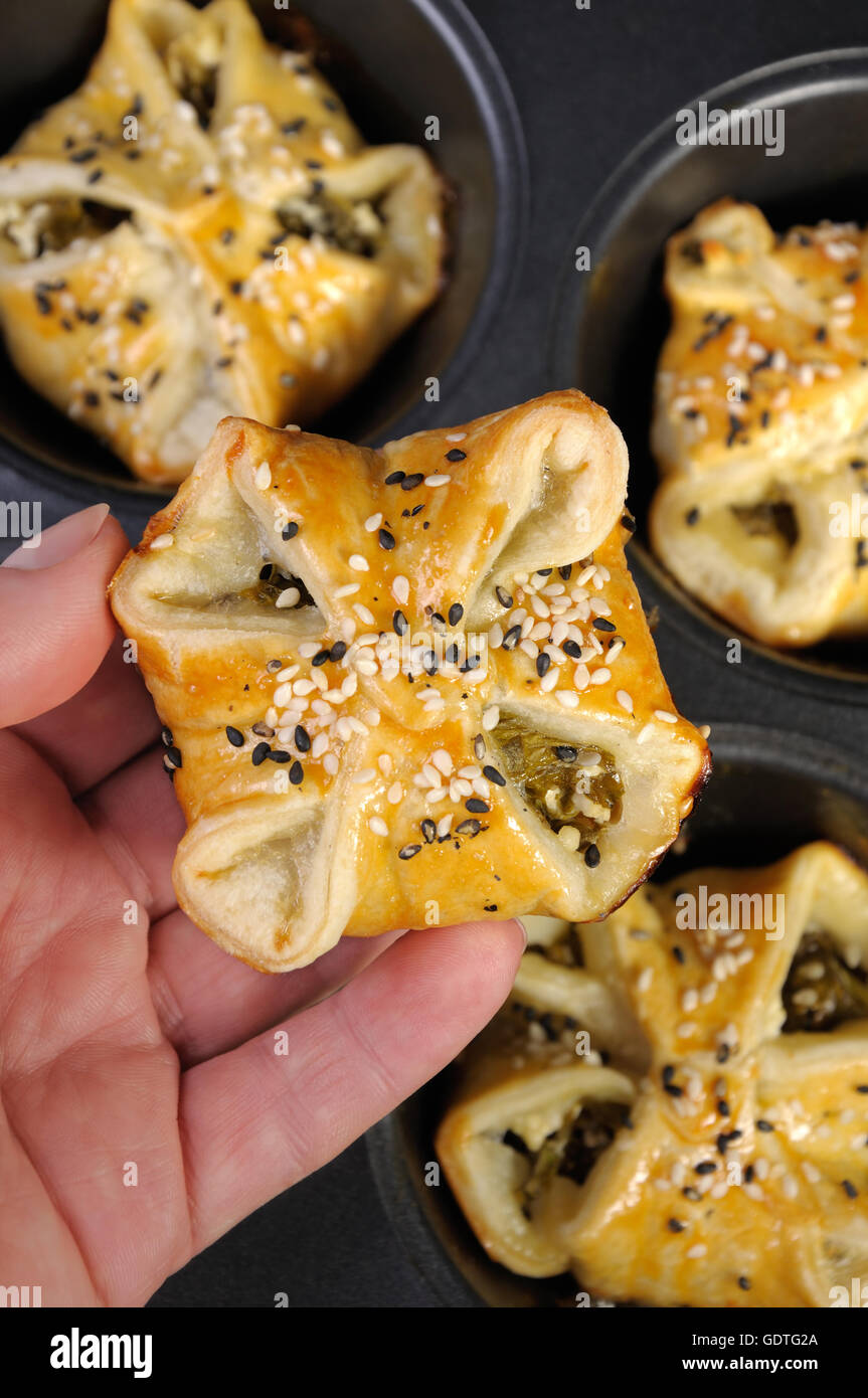 Bun pasta sfoglia con spinaci e ricotta in una mano su uno sfondo di vassoi la cottura Foto Stock