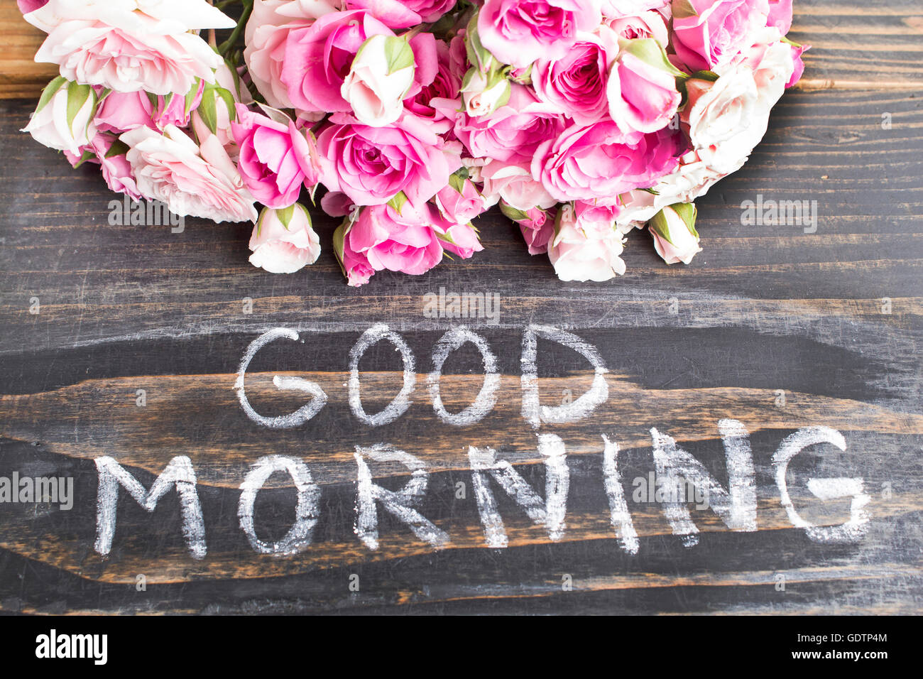 Parole di buona mattina con le rose rosa su un rustico sfondo di legno. Foto Stock