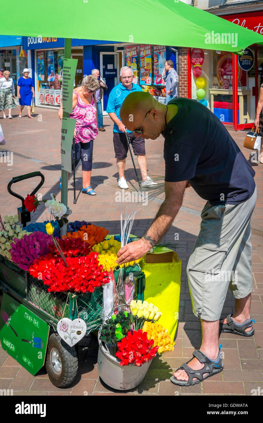 Uomo con un piccolo mercato di vendita di stallo rose artificiali Foto Stock