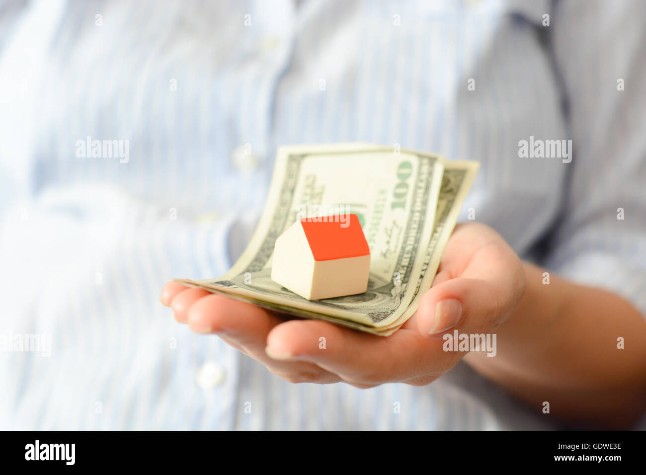 Donna mano azienda casa e denaro suggerendo il crescente costo della home prezzi Foto Stock