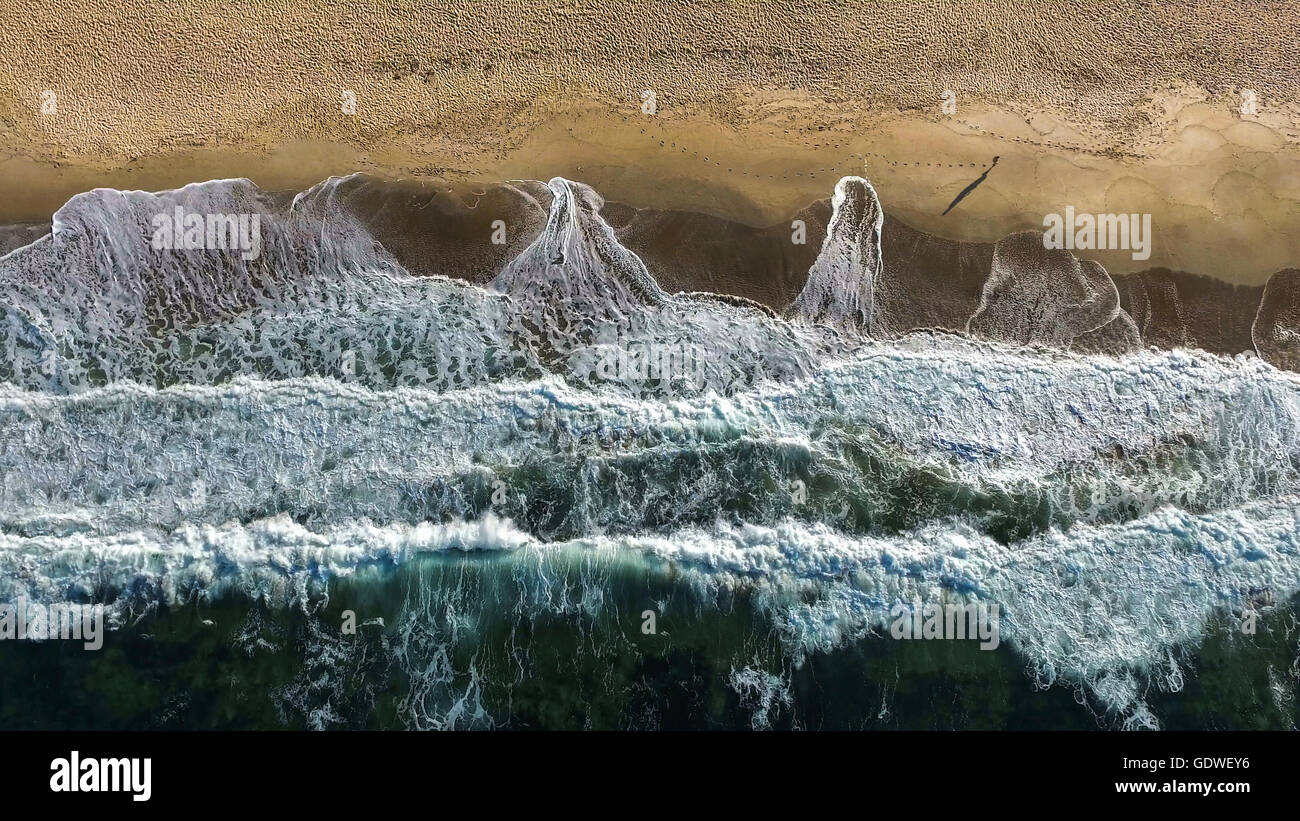 Immagine aerea di uomo che cammina su una spiaggia con onde di frantumazione. Foto Stock