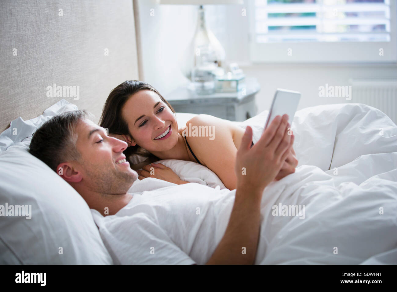 Coppia sorridente che stabilisce nel letto con tavoletta digitale Foto Stock