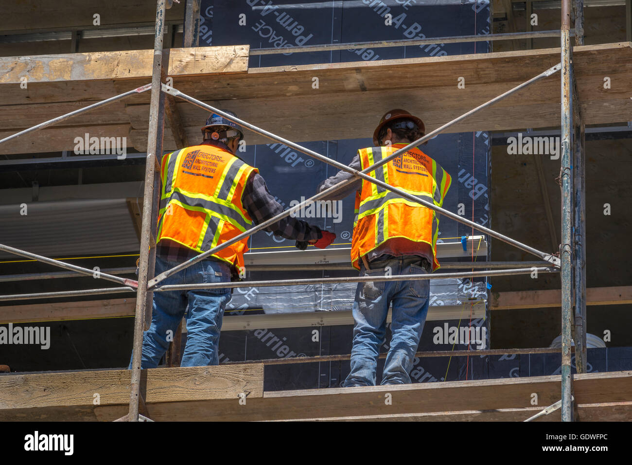 Due lavoratori in bright giubbotti di sicurezza in piedi sul ponteggio e lavorando su edificio in costruzione Foto Stock