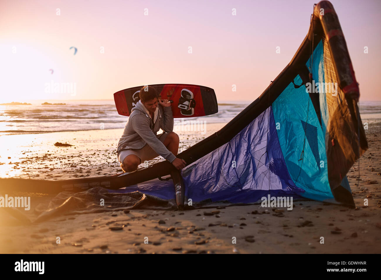 Uomo con kiteboarding attrezzatura sulla spiaggia al tramonto Foto Stock