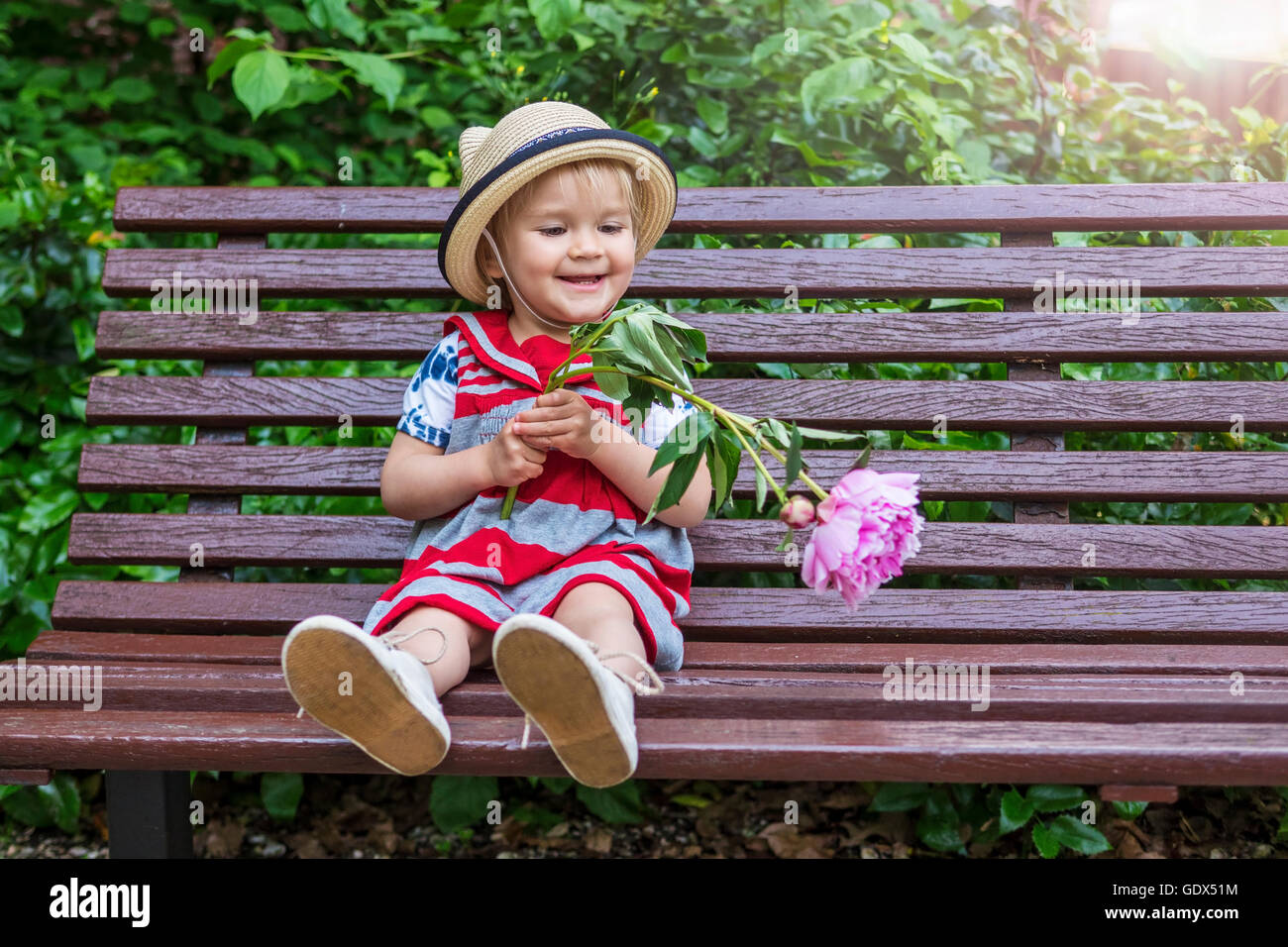 Incantevole piccola ragazza seduta su una panchina con un fiore Foto Stock