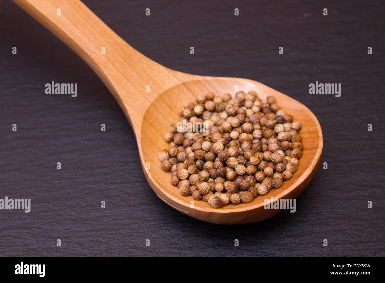 Il cucchiaio di legno con i semi di coriandolo su un pavimento di ardesia Foto Stock