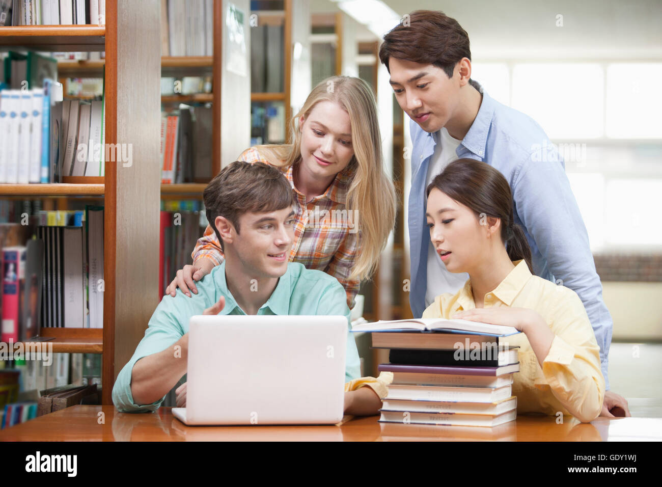 Quattro studenti universitari che studiano insieme utilizzando computer notebook e libri in biblioteca Foto Stock