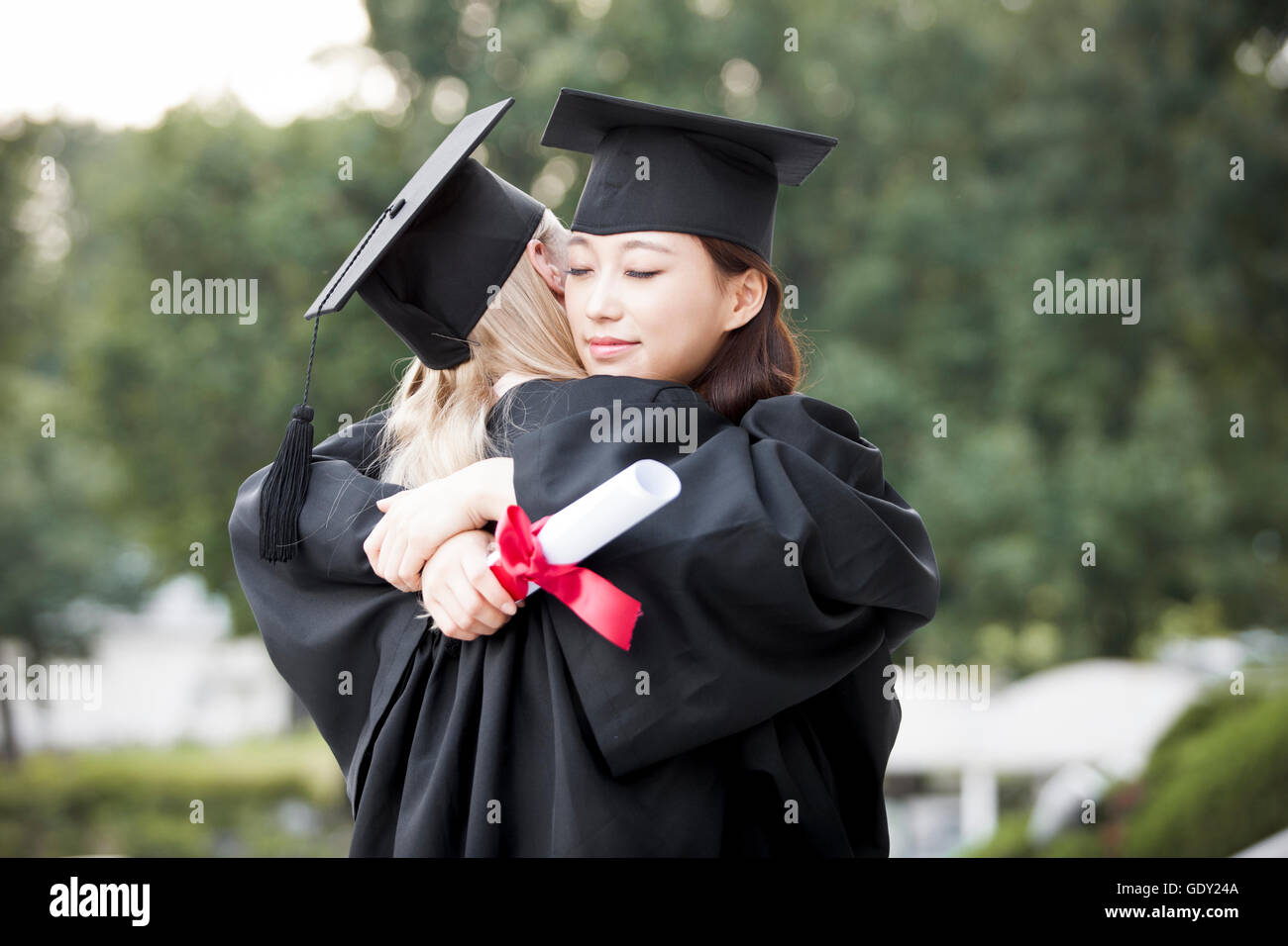 Vista laterale ritratto di due giovani donne laureati abbracciando chiudendo gli occhi Foto Stock