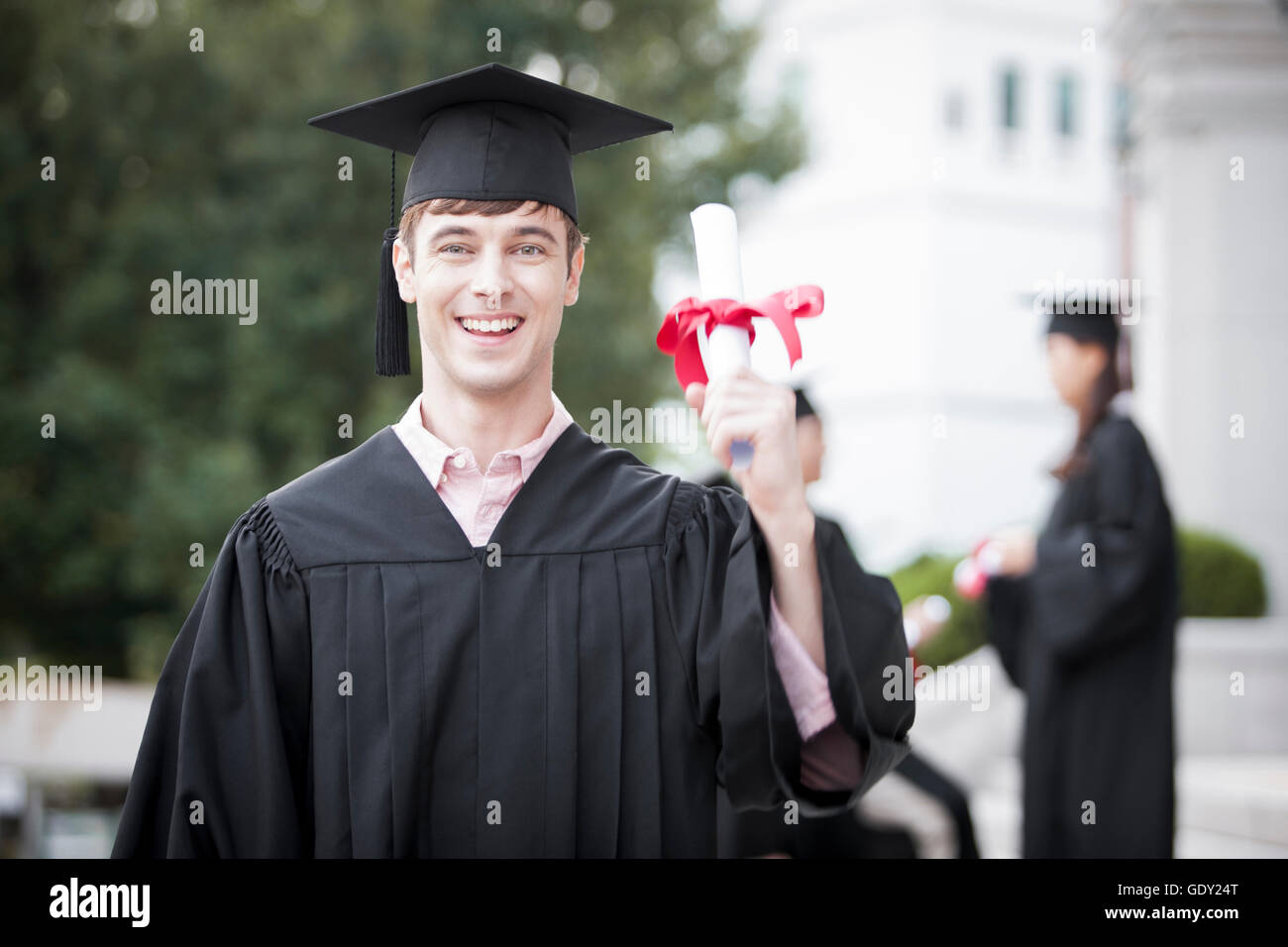 Ritratto di giovane laureato sorridente nel cappello e camice tenendo il diploma Foto Stock