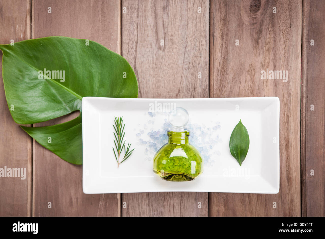 Bottiglia di cosmetici e lascia su di una piastra con foglia verde sul tavolo di legno Foto Stock