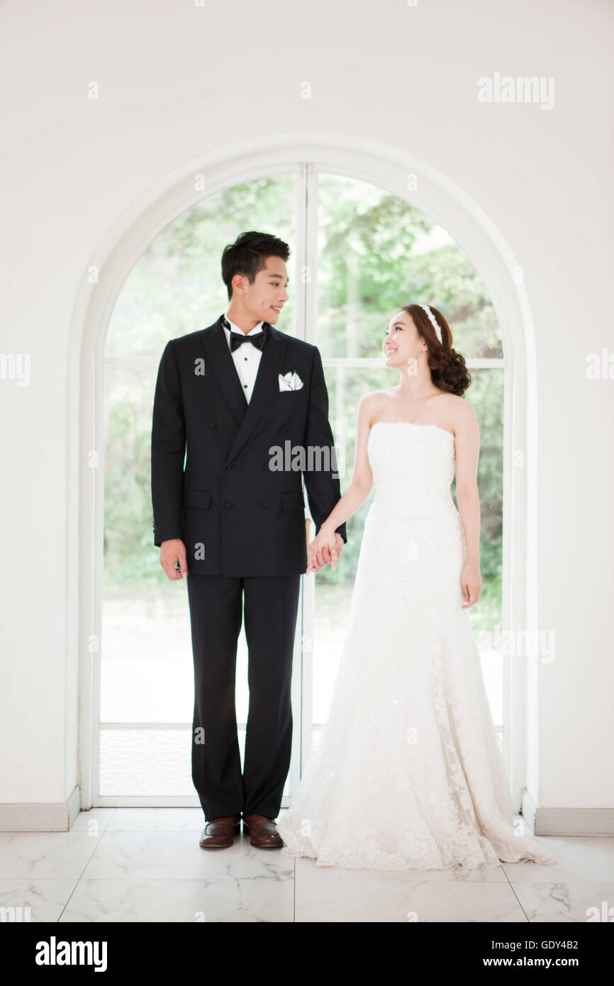 Sorridenti sposi in piedi tenendo le mani faccia a faccia Foto Stock