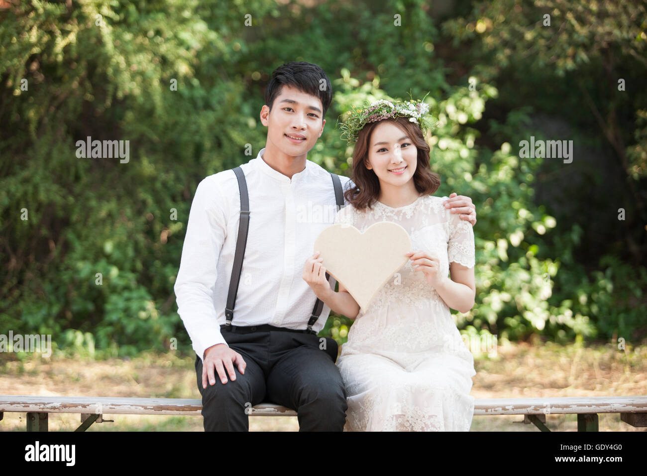 Sorridenti sposi seduta su una panchina con un cuore Foto Stock