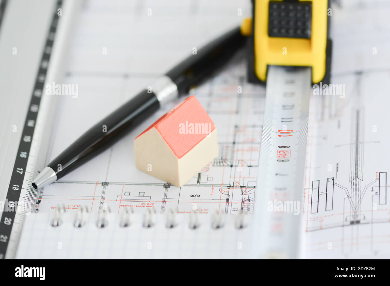 I piani di architettura di un edificio con un piccolo modello di casa sulla sommità del blueprint, penna, righello e notebook Foto Stock