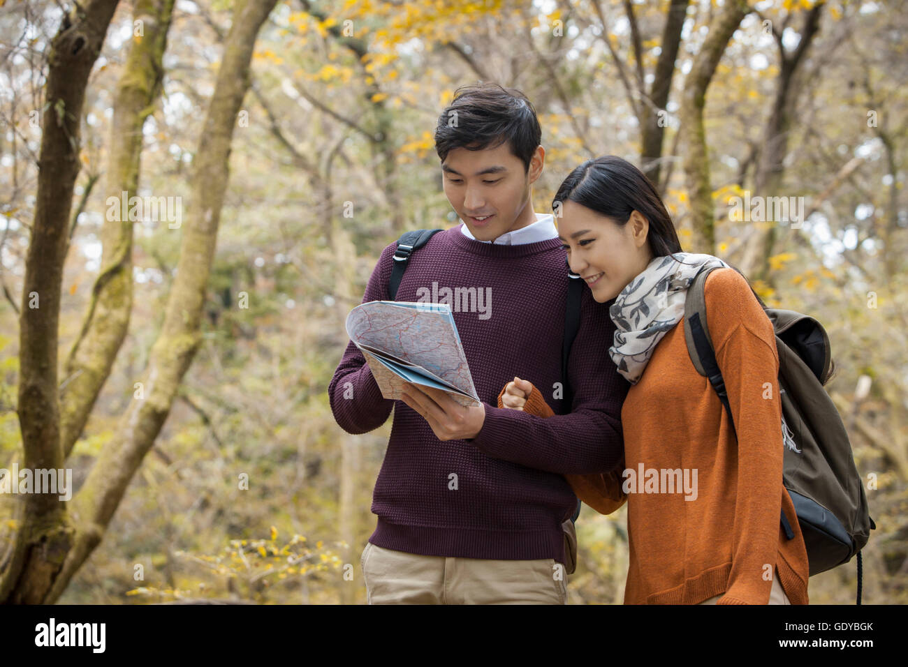 Giovane coppia sorridente trekking a braccetto la lettura di una mappa nel bosco in autunno Foto Stock
