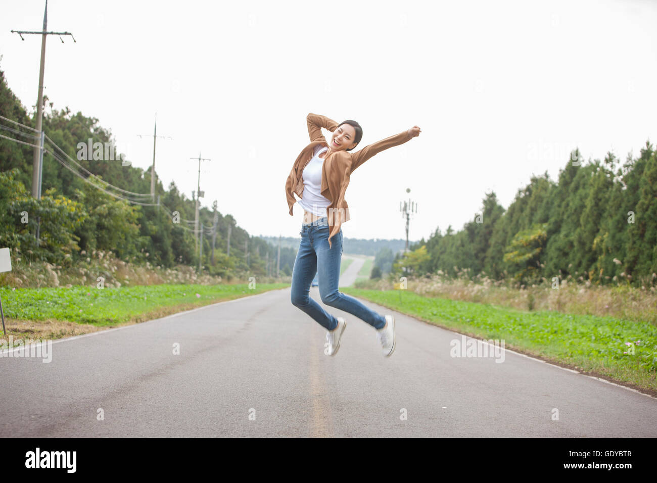 Giovane donna sorridente saltando su una strada alzando la mano Foto Stock