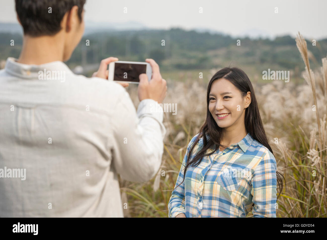 Ritratto di giovane donna sorridente in posa e uomo prendendo le foto di lei con una telecamera in color argento per il campo in erba Foto Stock