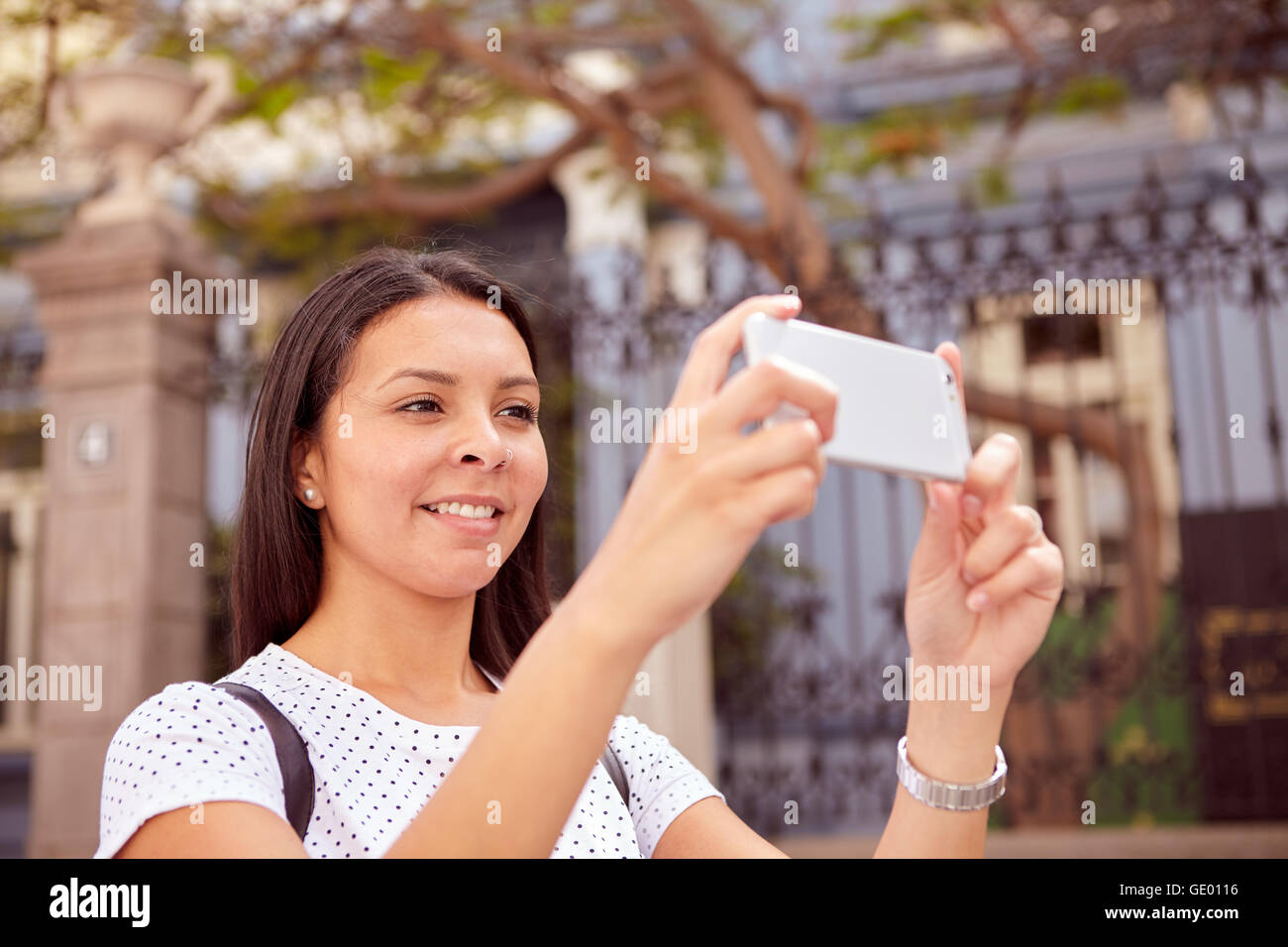 Ragazza giovane e carina a scattare foto con il suo telefono cellulare mentre in piedi di fronte a vecchi edifici, indossando i suoi capelli sciolti e a spo Foto Stock